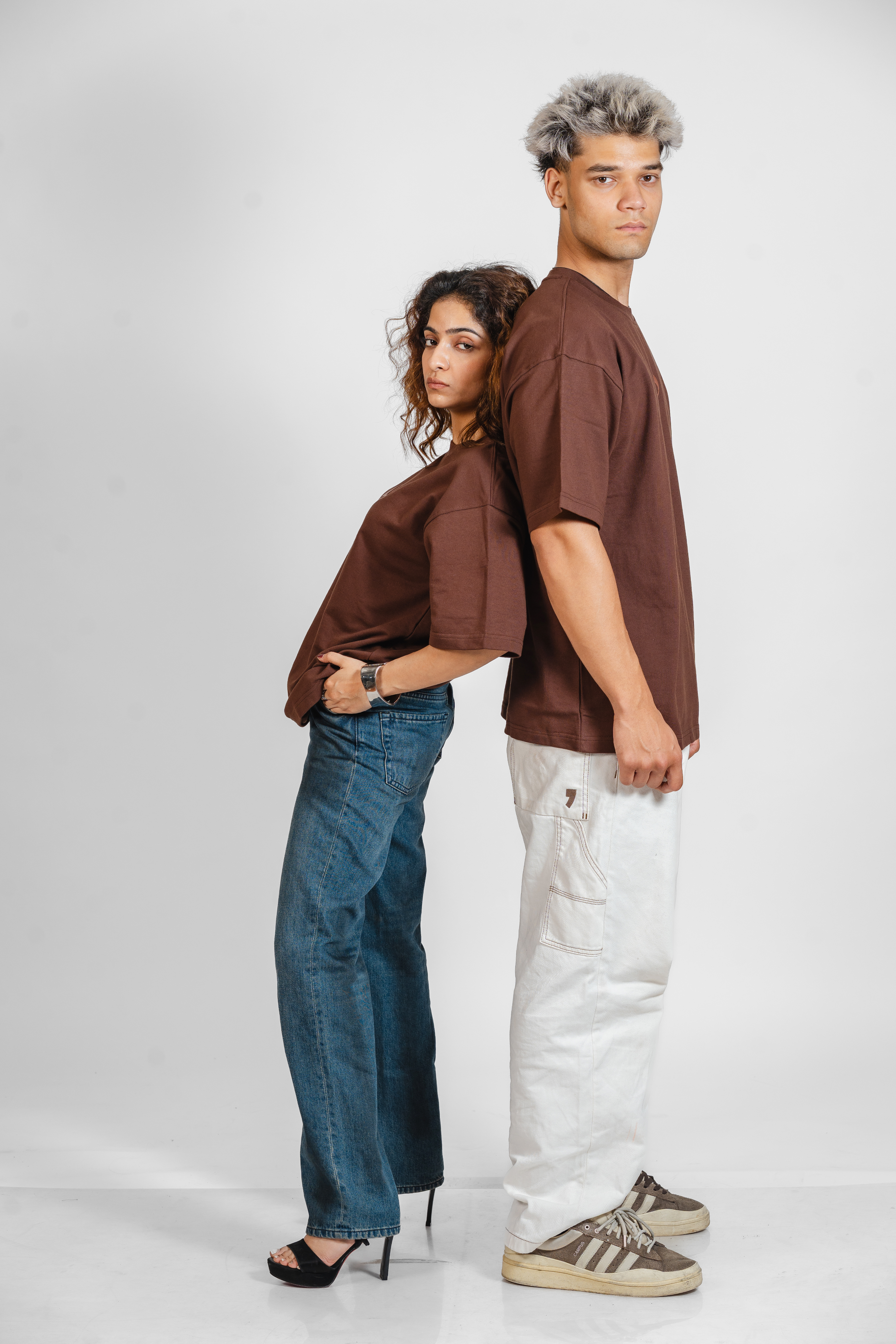 Two people wearing brown shirts and jeans standing back-to-back on a white background