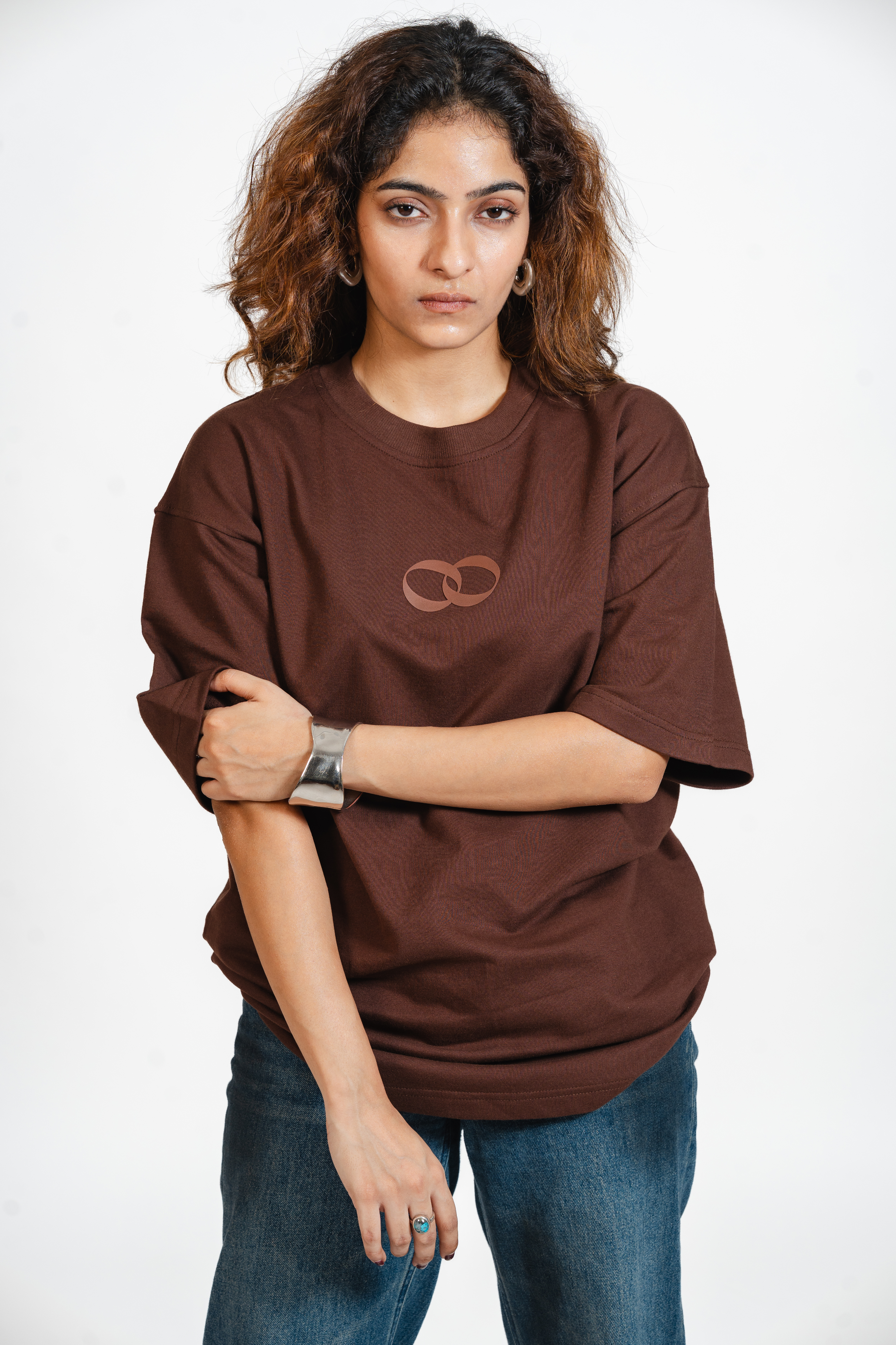 Woman wearing a brown t-shirt with the one more please logo on a white background
