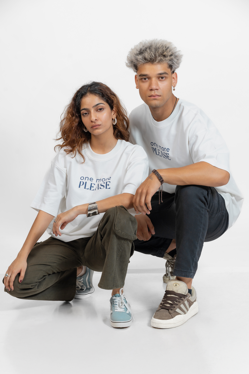 Two people wearing white t-shirts with text that says 'One More Please' in blue, sitting on a white background