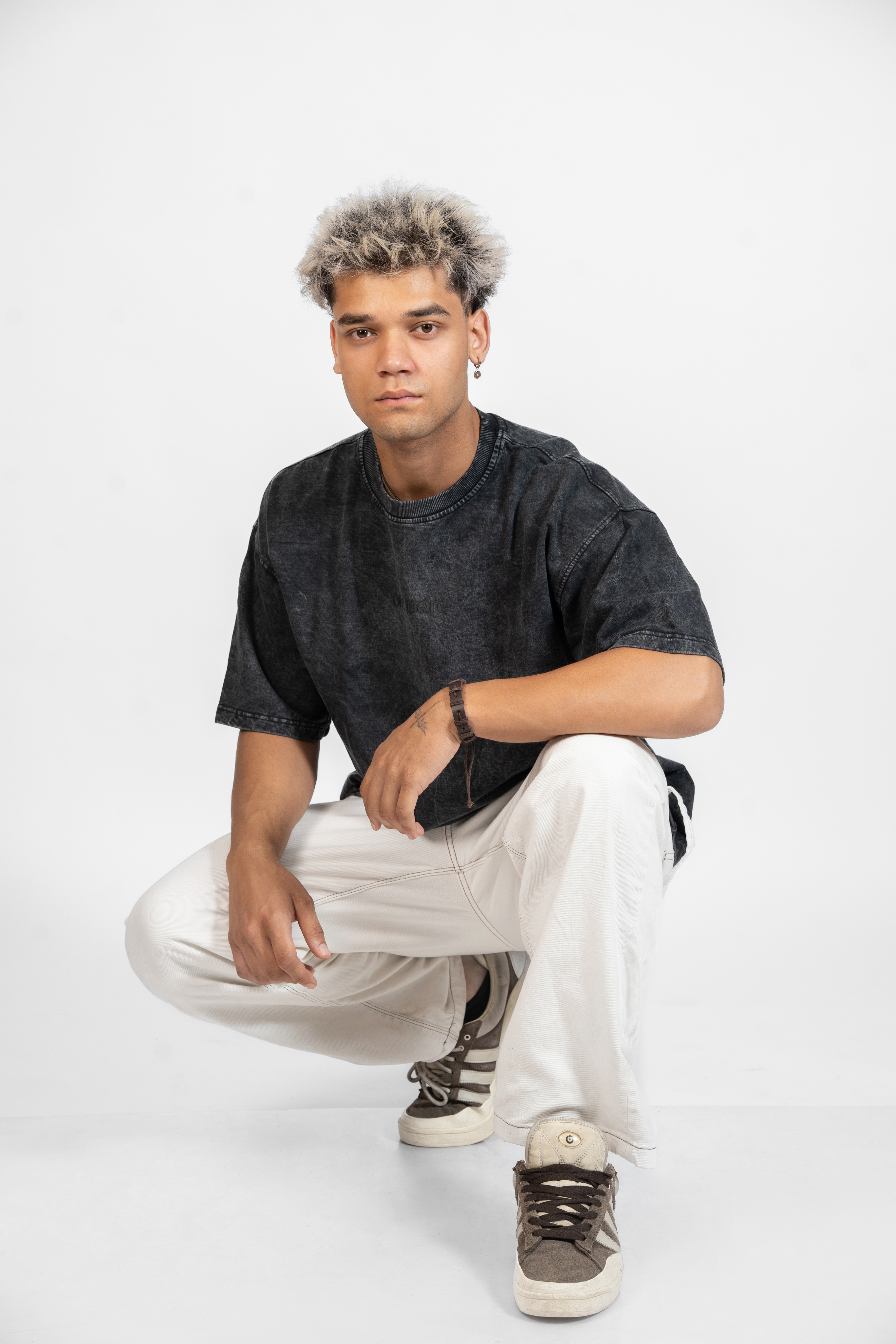 Man wearing a black t-shirt, white pants, and dark shoes on a white background