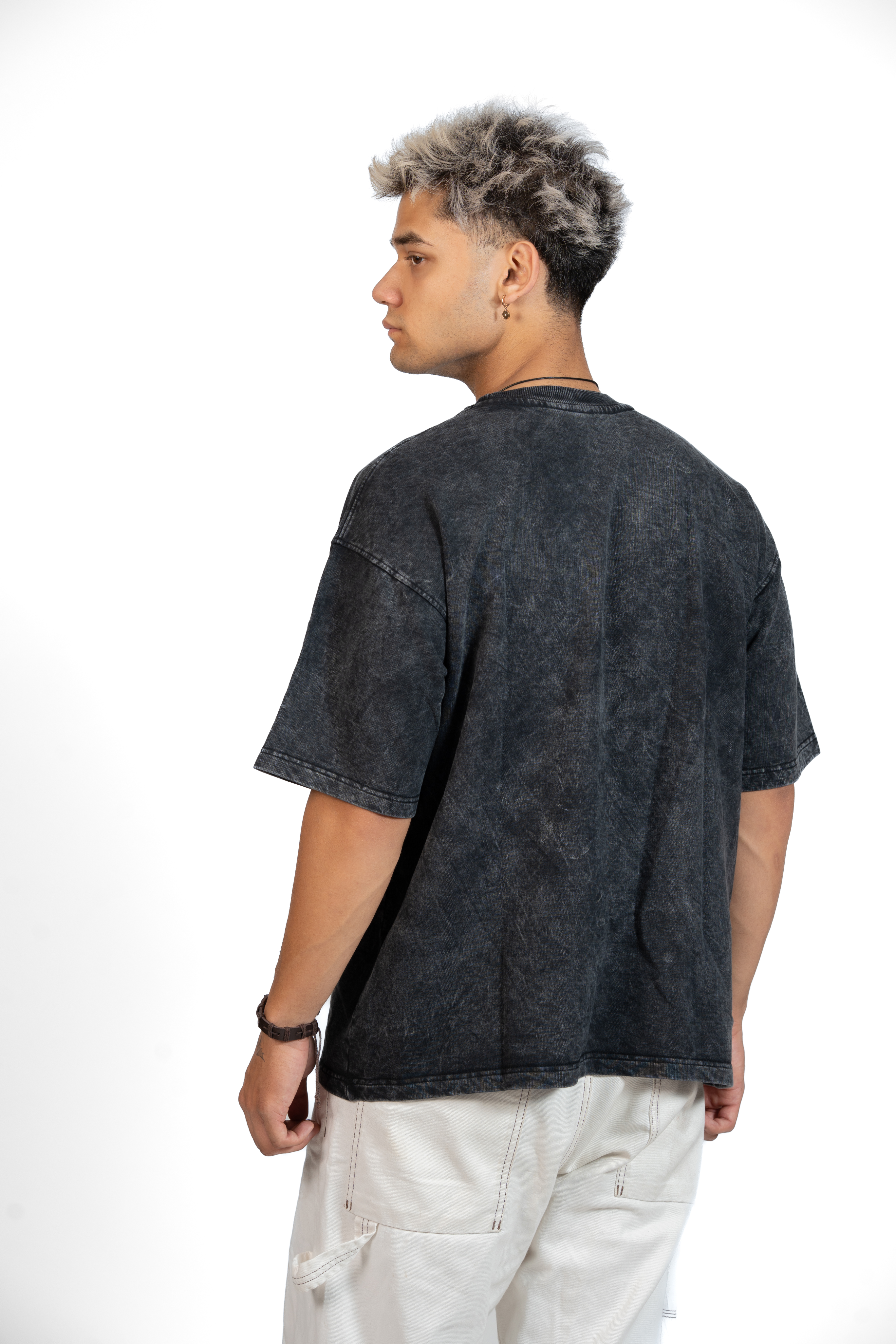 Man wearing a dark tie-dye t-shirt and white pants facing backwards on a white background