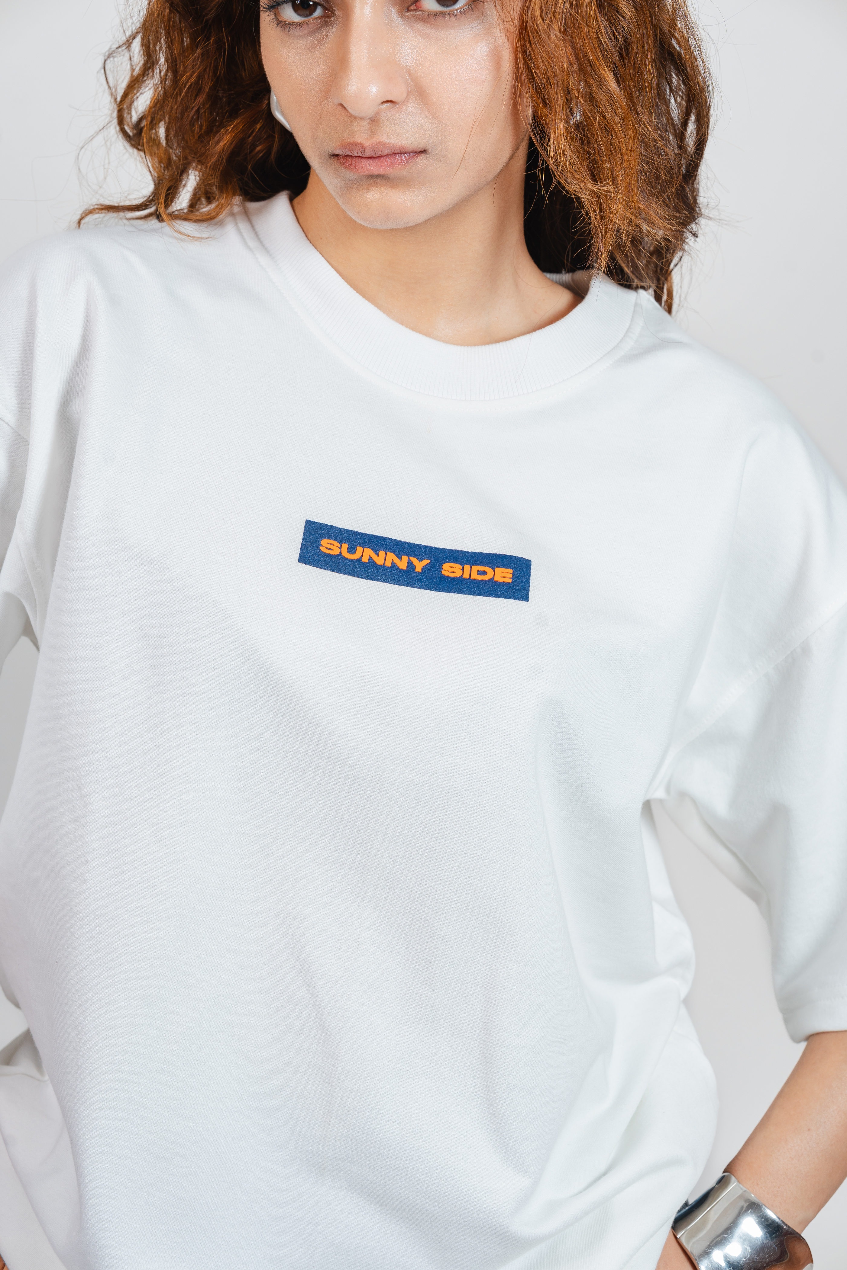 Woman wearing a white oversized shirt with the text 'Sunny Side' on the chest