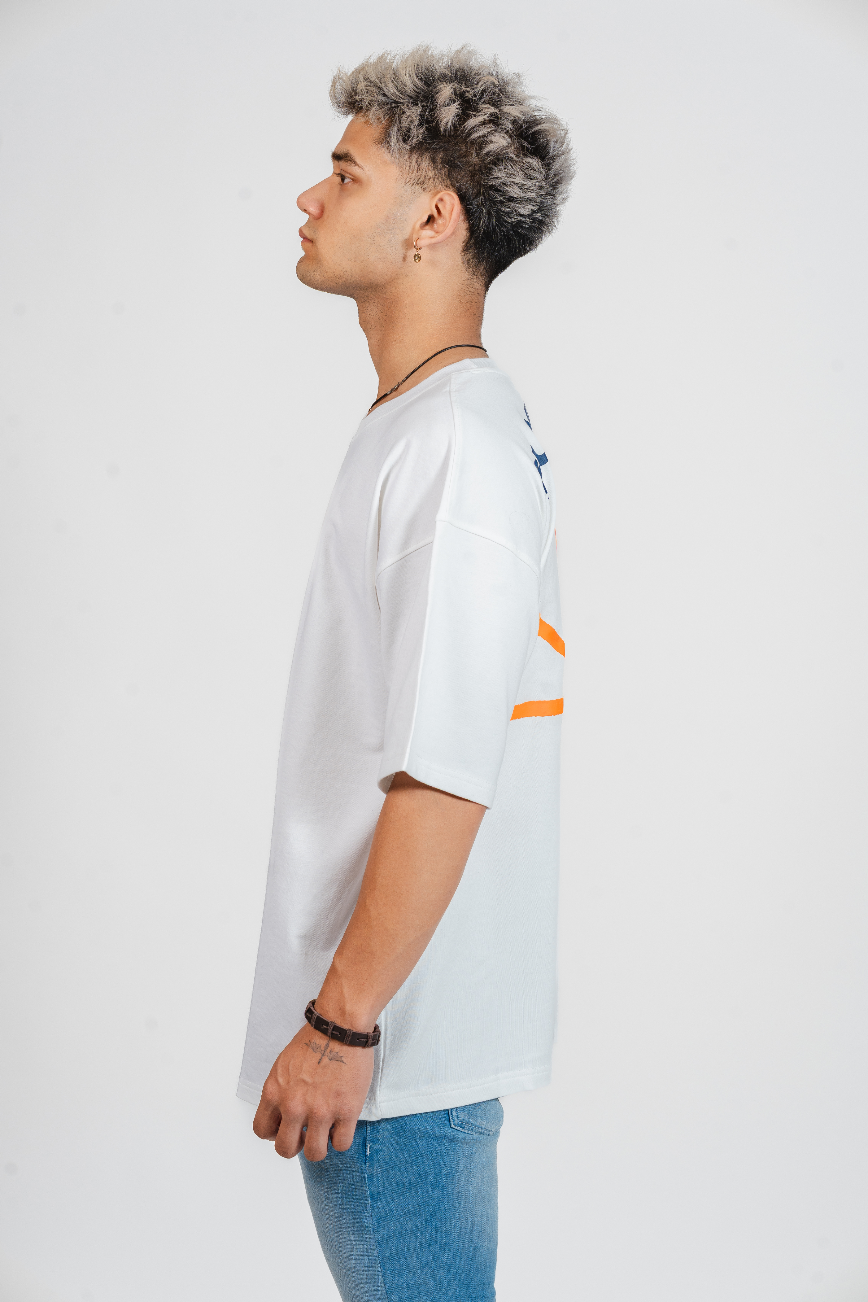 Man wearing a white t-shirt with an orange and blue design on the back on a plain background facing sideways.