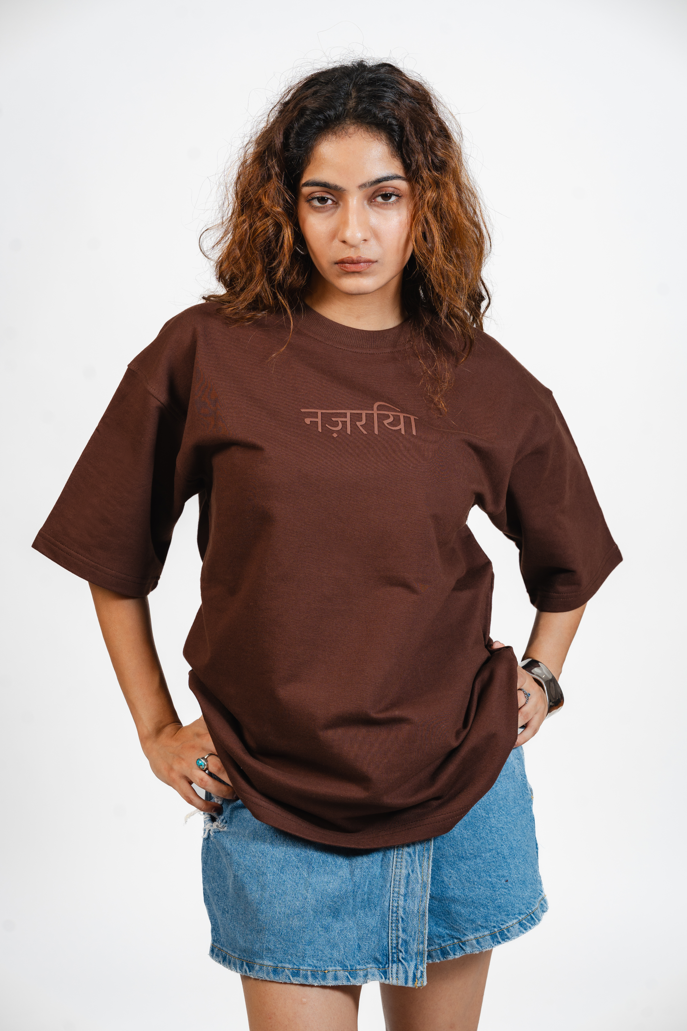Woman wearing a brown t-shirt with Hindi text that says 'Nazariya' and a denim skirt on a white background