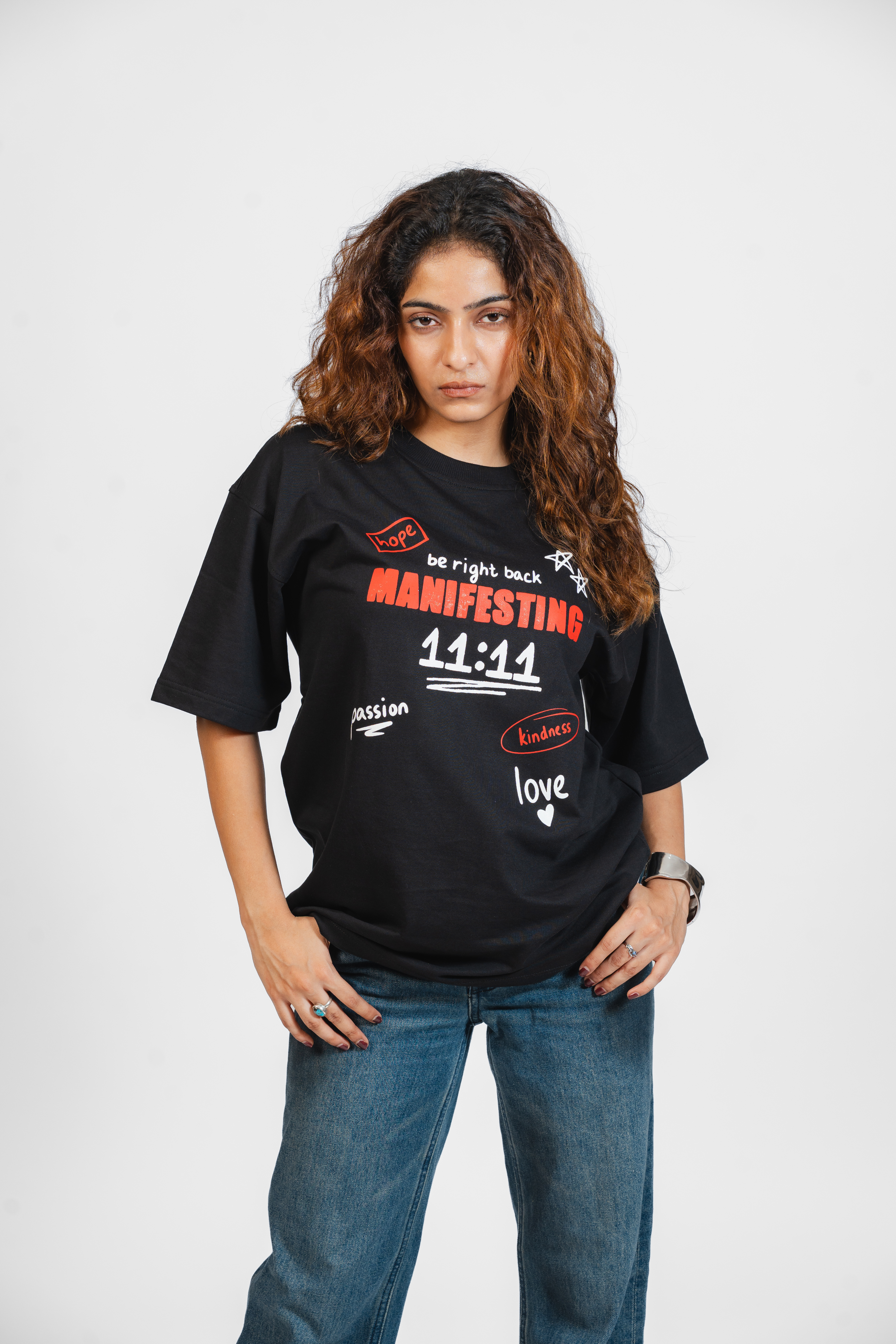 Woman wearing a black t-shirt with text that says 'Manifesting' in red and other graphics on a white background