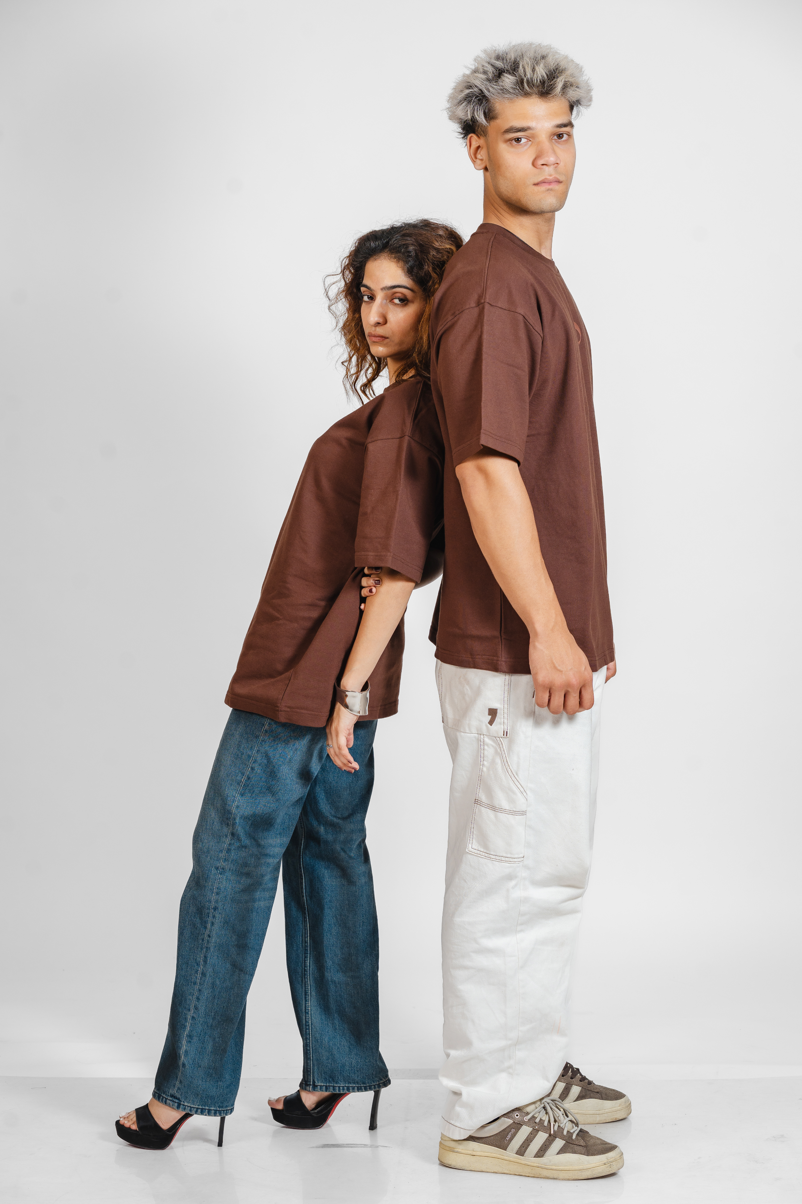 Two people wearing matching brown tshirts and jeans on a white background