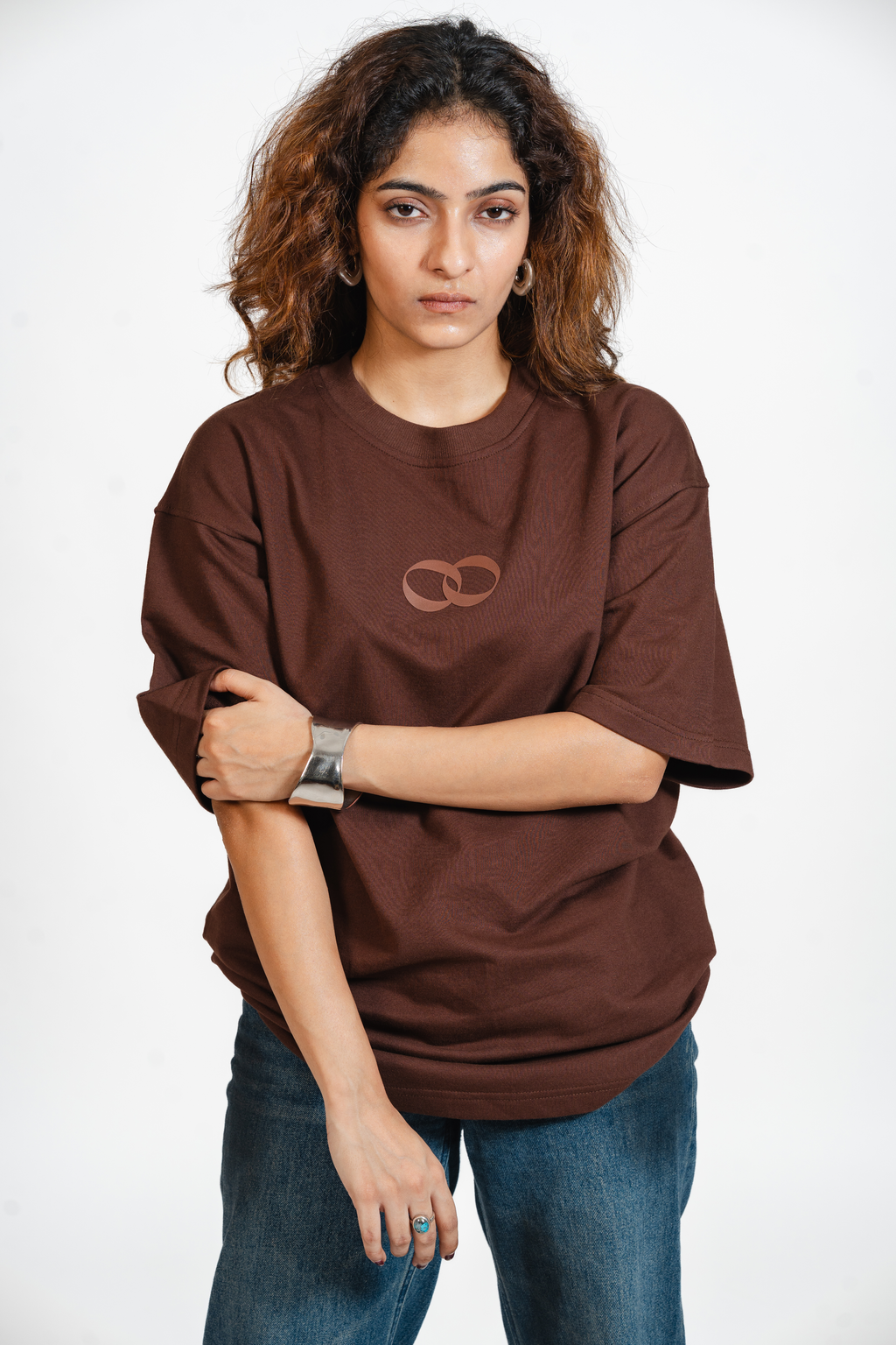 Woman wearing a brown t-shirt with the one more please logo on a white background
